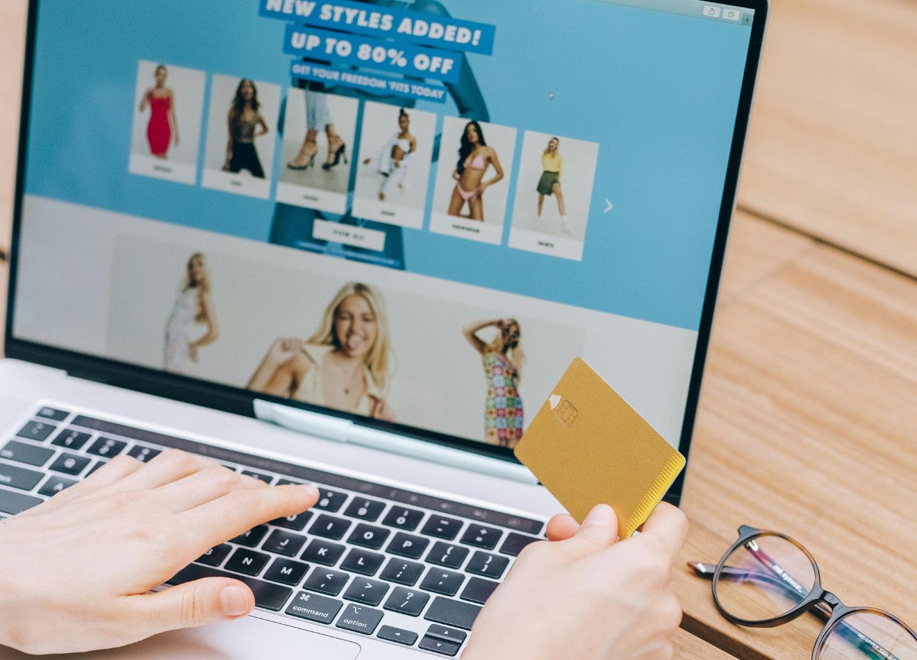 Image of a laptop being used to buy something from an eCommerce store. A woman's hand holding a credit card are visible over the keyboard